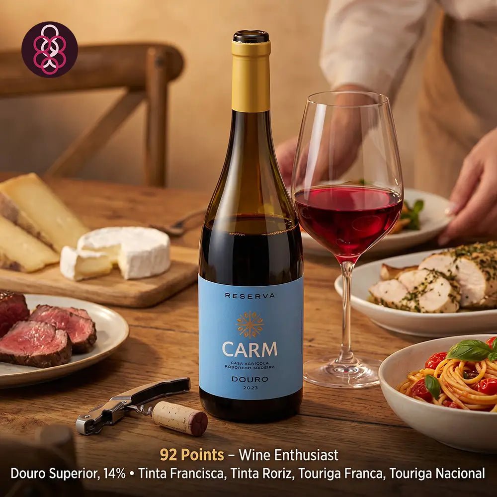 A bottle of Carm Reserva Douro red wine stands on a wooden dining table beside a filled wine glass and plated food, with a person partially visible in the background. The bottle label reads 'Reserva Carm' and 'Douro 2023'.