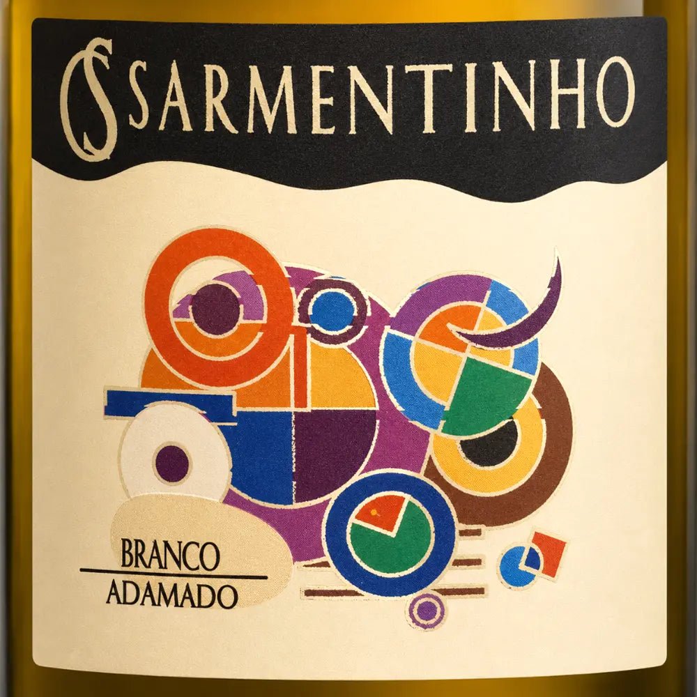 Close-up of a wine bottle label reading 'SARMENTINHO' and 'BRANCO ADAMADO', with a cream background and colorful abstract geometric artwork in orange, purple, blue, green, yellow, and brown.