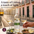 A bottle of Sotta white wine is displayed on a table with two filled wine glasses, olives, cheese, and a corkscrew in a street setting. Text at the top reads 'A taste of Lisbon, a touch of light.