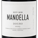 Close-up of a white wine label for Manoella Douro 2023, with black text and a dark bottle edge visible around the label.