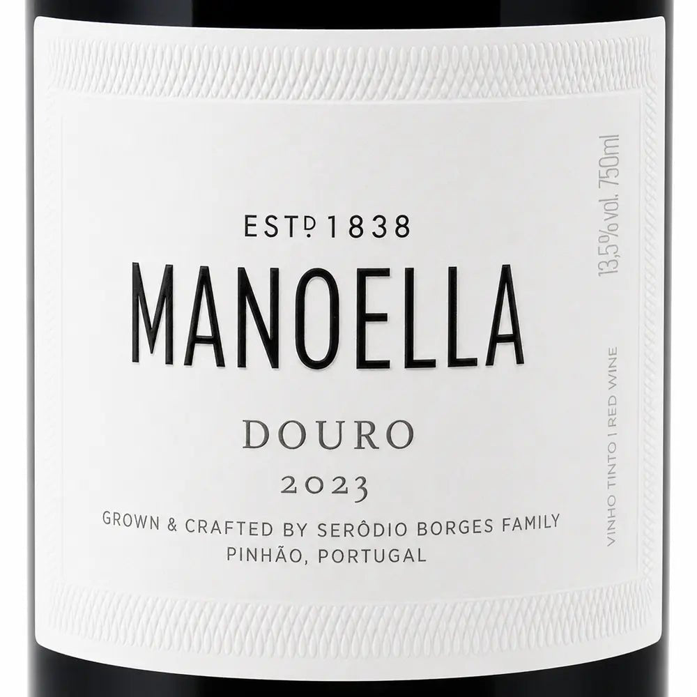 Close-up of a white wine label for Manoella Douro 2023, with black text and a dark bottle edge visible around the label.