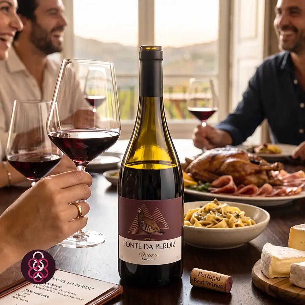 A bottle of Fonte da Perdiz red wine stands on a dining table, surrounded by wine glasses, a roasted turkey, pasta, cheese, and two men smiling in the background.