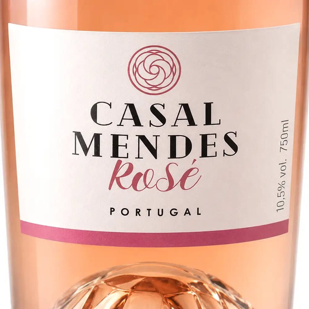 Close-up of a rosé wine bottle label reading 'CASAL MENDES Rosé PORTUGAL' with the rosé liquid visible through the clear bottle and a faceted glass base.