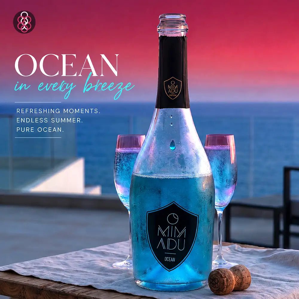 A bottle of Mimadu Ocean sparkling beverage in a blue iridescent tone, styled on a table with two pink-tinted glasses and two corks against an ocean backdrop at sunset. Text on the left reads 'OCEAN in every breeze' with descriptive copy.