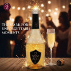 A bottle of Mimadu sparkling wine or champagne with a black label and gold liquid, shown on a wooden table beside a filled champagne flute, with sparklers around the bottle and a blurred party scene in the background. Text on the left reads 'THE SPARK FOR UNFORGETTABLE MOMENTS' with the Mimadu logo at top left.