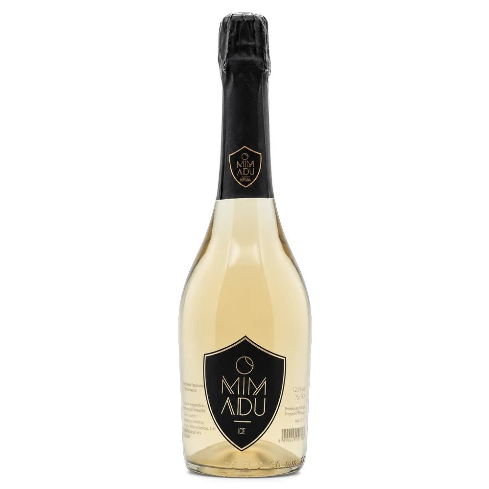 A bottle of Mimadu sparkling wine with a pale golden-amber liquid, a black foil capsule, and a black shield-shaped label on a plain white background.
