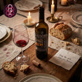 Wine bottle and glass on a table with bread and candles, featuring Alfacinha Reserva red wine branding.