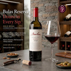 A bottle of Bulas Douro Reserva red wine stands on a stone table beside a filled wine glass, with a cork, olives, and a corkscrew nearby. The background shows a wine cellar setting with shelves and bottles, and the left side includes promotional text for the Bulas Reserva wine.