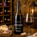 A bottle of Ramilo red wine with a glass filled with red wine, set on a rustic wooden table with cheese, cured meat, and a cork.
