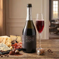 Bottle of Aphros Yakkos wine with a glass of red wine on a wooden table with cheese and nuts.