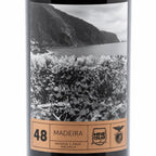 A bottle of Madeira wine with a black-and-white scenic label showing a coastal vineyard and mountains, plus a tan band at the bottom with the text '48 MADEIRA', 'RESERVA 5 ANOS MALVASIA'.