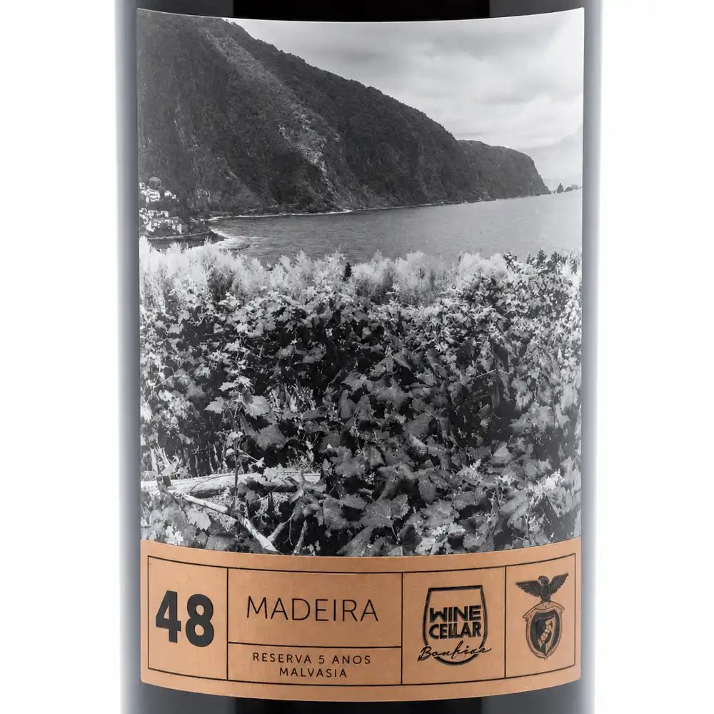 A bottle of Madeira wine with a black-and-white scenic label showing a coastal vineyard and mountains, plus a tan band at the bottom with the text '48 MADEIRA', 'RESERVA 5 ANOS MALVASIA'.