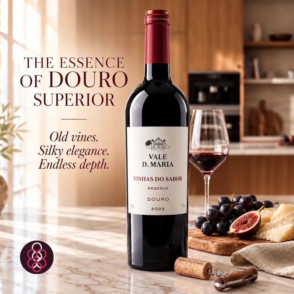 A bottle of Vale D. Maria Vinhas do Sabor Reserva Douro red wine stands on a kitchen counter beside a filled wine glass, grapes, figs, cheese, and a corkscrew, with promotional text reading 'The Essence of Douro Superior.