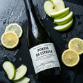 Wine bottle labeled 'Portal da Estrela white wine' with sliced apples and lemons on a dark surface