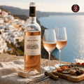 A bottle of Arca Nova Vinho Verde rosé wine stands on a stone surface beside two filled wine glasses, a cork, a corkscrew, and a small food board with olives, tomatoes, and fish, set against a blurred coastal hillside and sea background. The Arca Nova logo appears in the top-right corner.