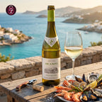 A bottle of Arca Nova white wine stands on a wooden table beside a glass of white wine, with a plate of seafood and a corkscrew in the foreground. The background shows a scenic coastal view with blue water and mountains at sunset.