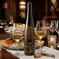 A bottle of Conde de Villas Alvarinho white wine stands on a dining table with two filled wine glasses, a plate of oysters and shrimp, and a corkscrew in a softly lit restaurant setting.