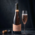 Bottle of Rosé Almanac Brut with a glass of champagne on a dark background