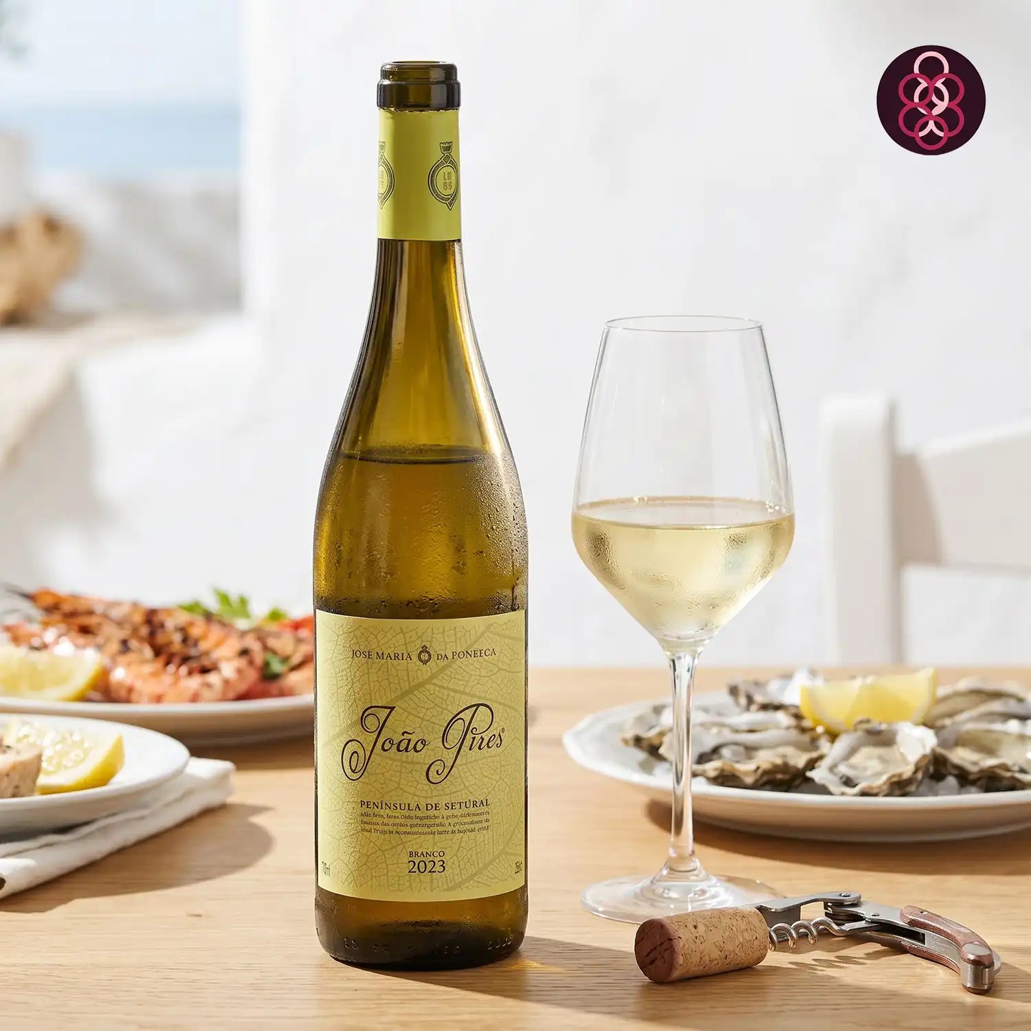 Bottle of João Pires white wine with a glass on a table with food in the background