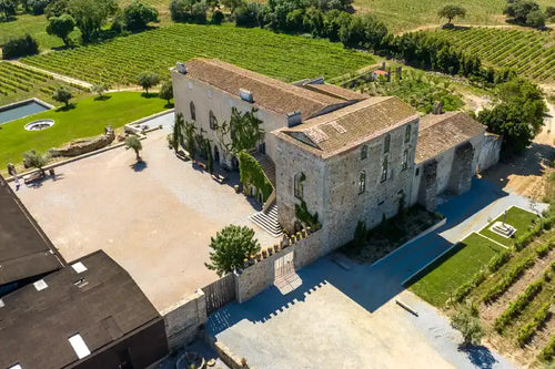 Macanita_Winery. Aerial view of a large stone villa with a courtyard, surrounded by vineyard fields and green landscaping.