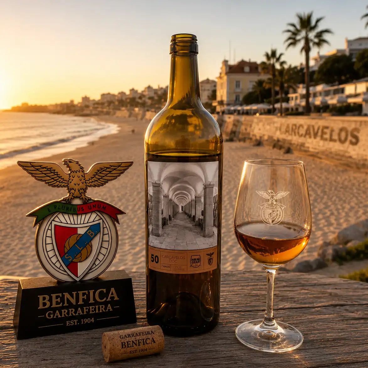 Bottle and glass of Benfica wine with a decorative emblem on a beach at sunset.